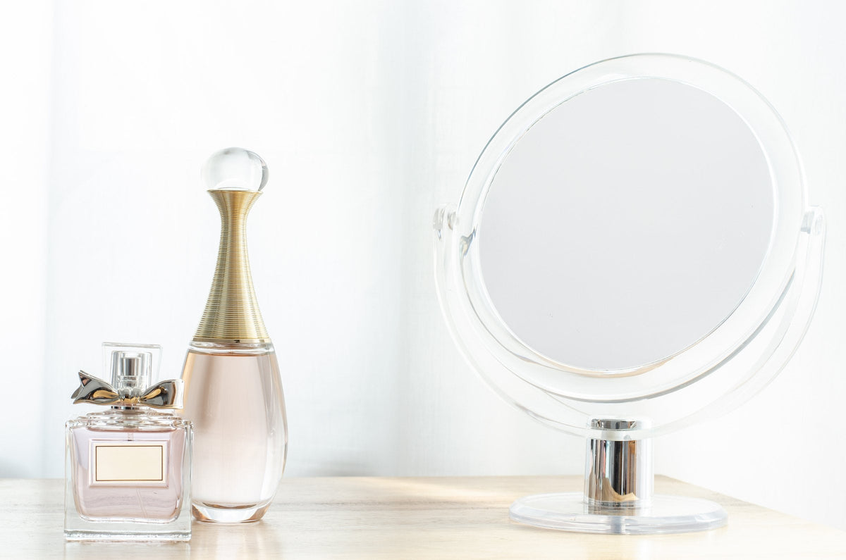 Dior perfume bottles beside a round mirror on a pale dressing table