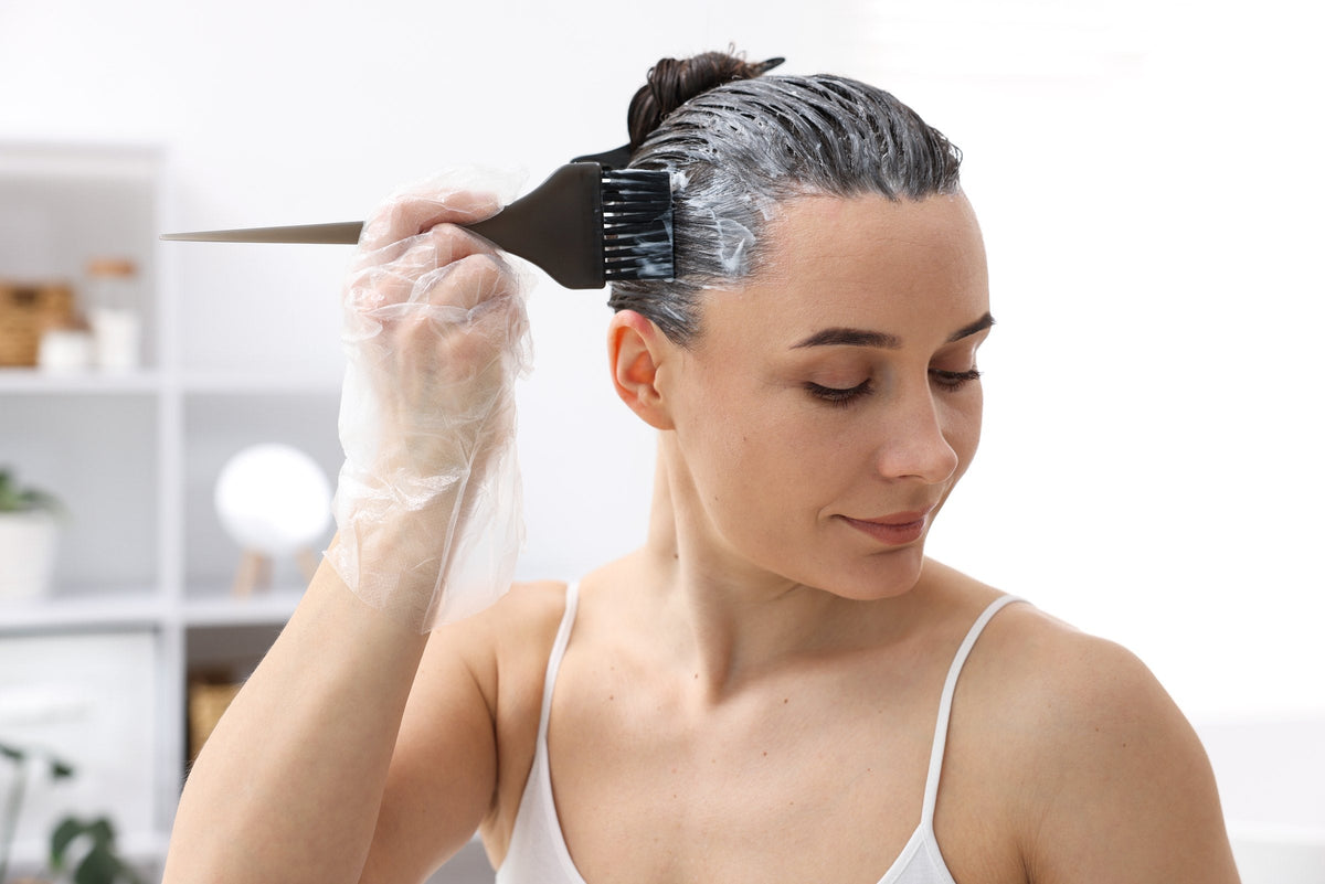 A woman brushing hair colour onto her roots at home