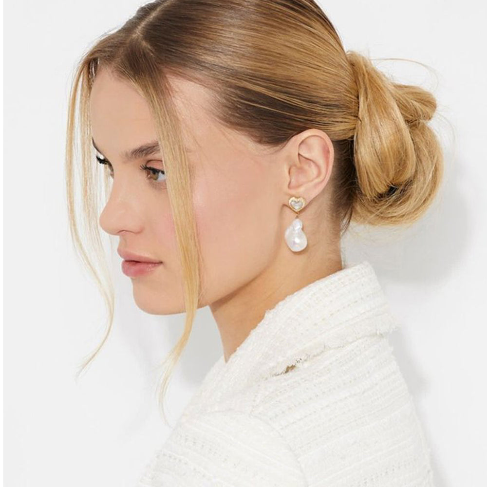 Gold heart stud earrings with pavé stones and hanging white pearl drops on white background